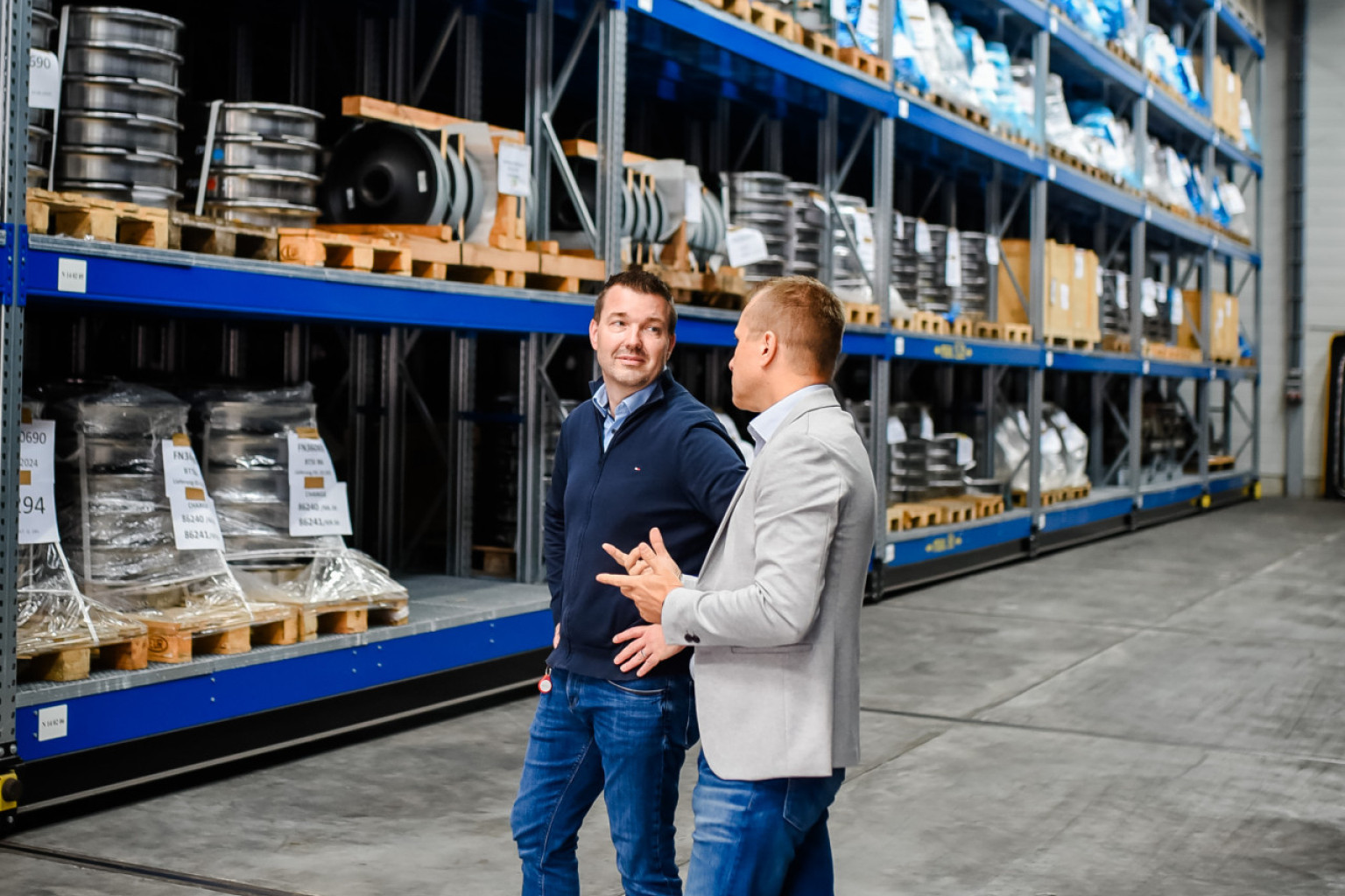 Zwei Mitarbeiter stehen in einem unserer Lagerdepots. Im Hindergrund sind Hochregale zu sehen.