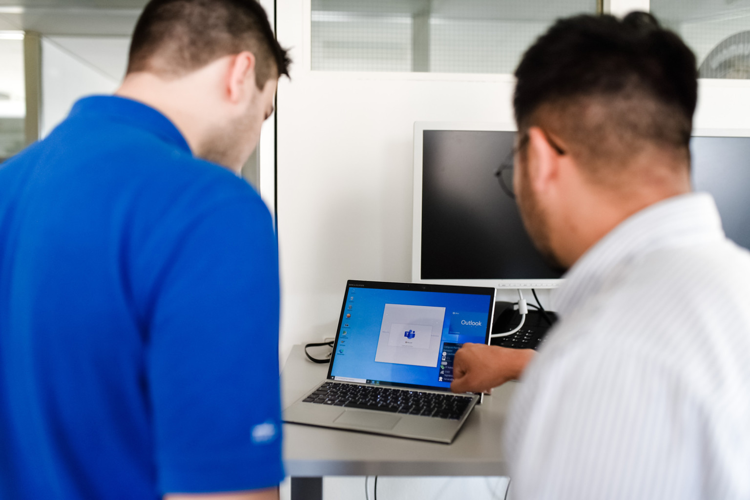 Ein Mitarbeiter erklärt einem Kollegen etwas an seinem PC.