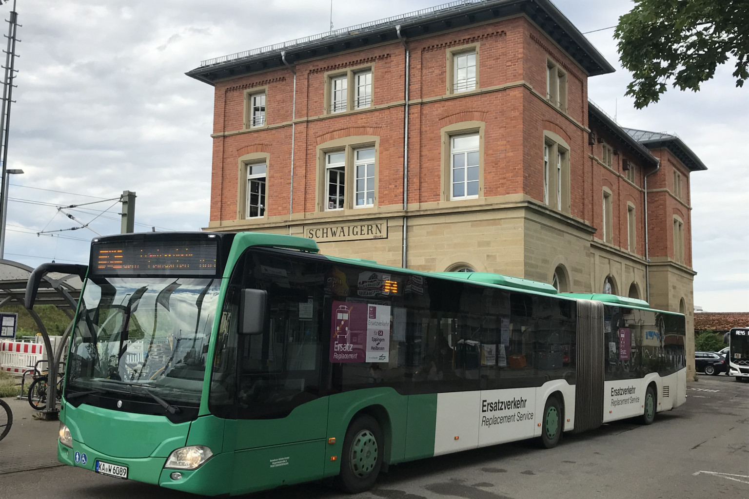Ein grüner SEV Bus steht vor einem Backsteingebäude.