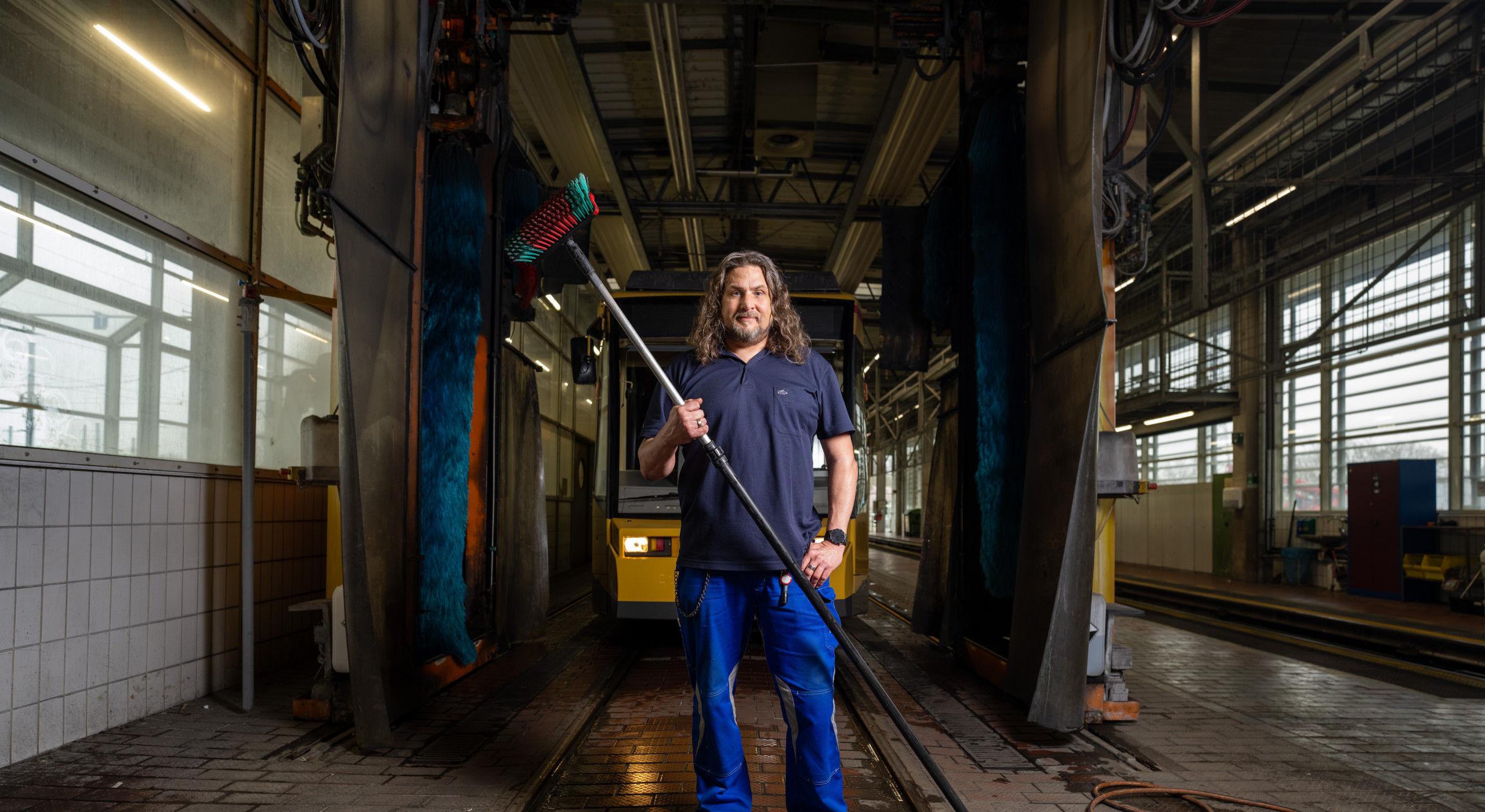 Ein Mann mit längeren Haaren steht in der Waschhalle für Bahnen mit einem langen Reinigungsstab in der Hand