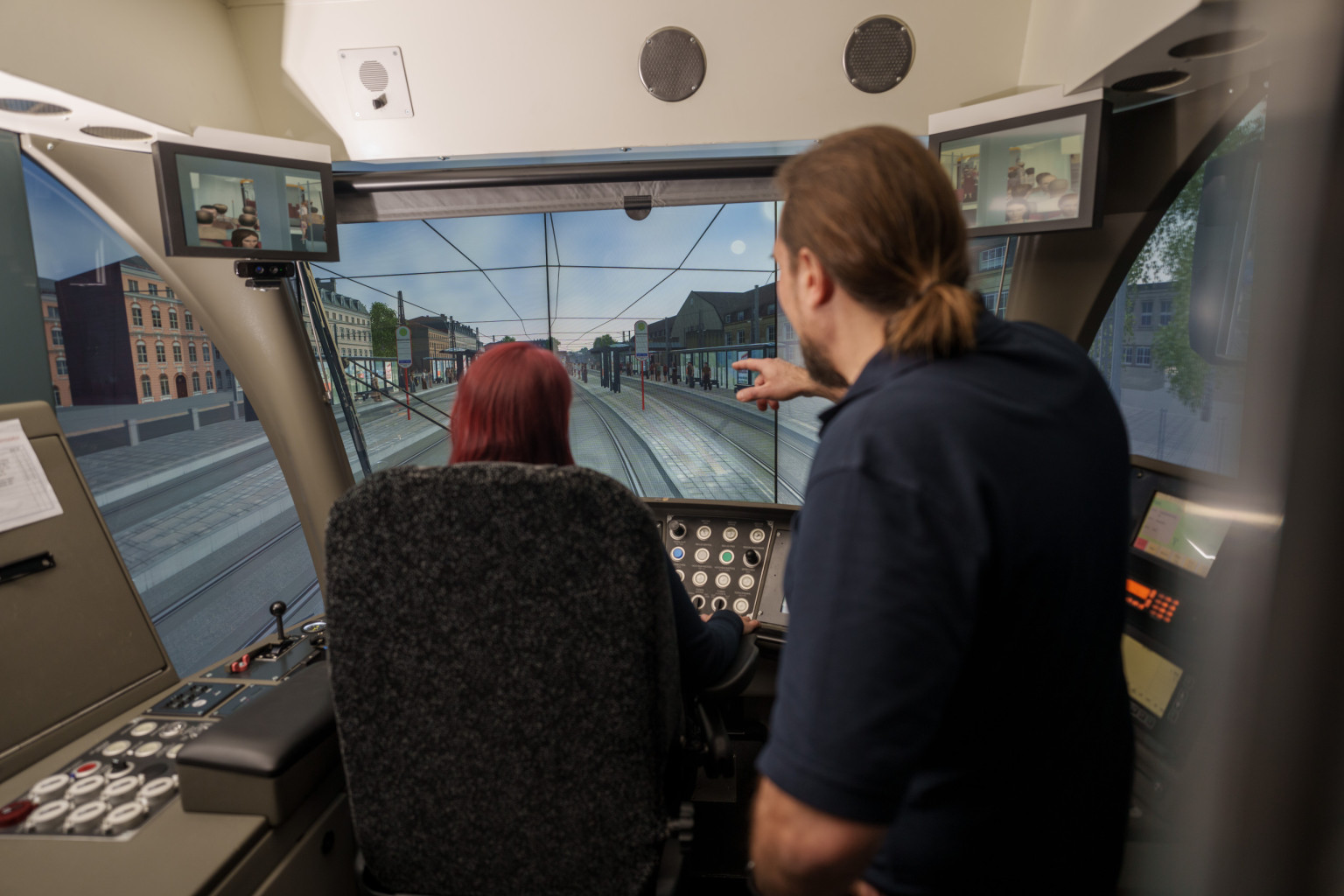 Ein Ausbildungsleiter erklärt einer künftigen Fahrerin etwas am Bahnfahrsimulator.