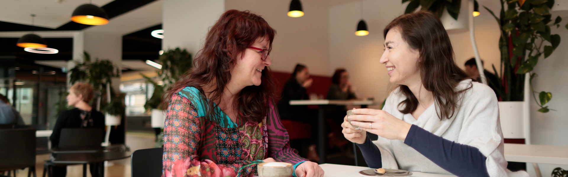 Zwei Mitarbeiterinnen tauschen sich bei einem Kaffee im Nahverzehr aus.
